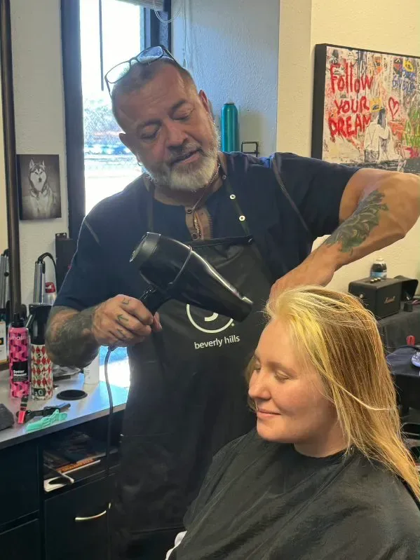 Rob Maggart blow drying a client's hair in his Colorado Springs salon, both hands occupied